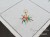Kolorowy haft ręczny na białej serwecie świątecznej z lnu, tworzący dekoracyjny akcent na stole.